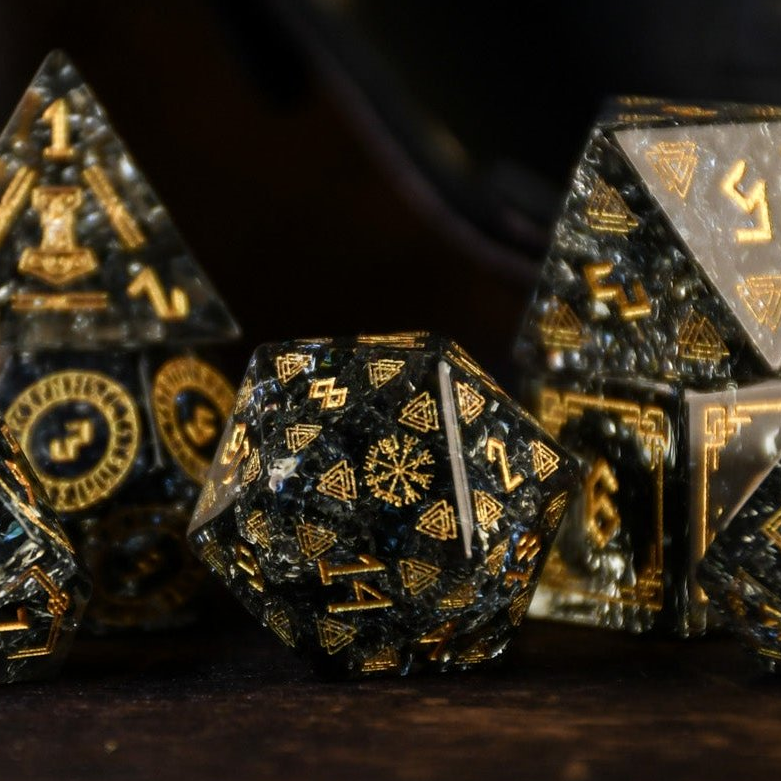 A set of black shattered glass polyhedral dice with Nordic designs, including one d4, one d6, one d8, two d10, one d12, and one d20, displayed on a wooden surface.