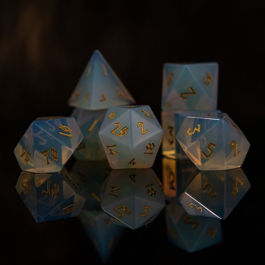A collection of hand-carved, opalescent white gemstone dice with engraved numbers, displayed against a black background.