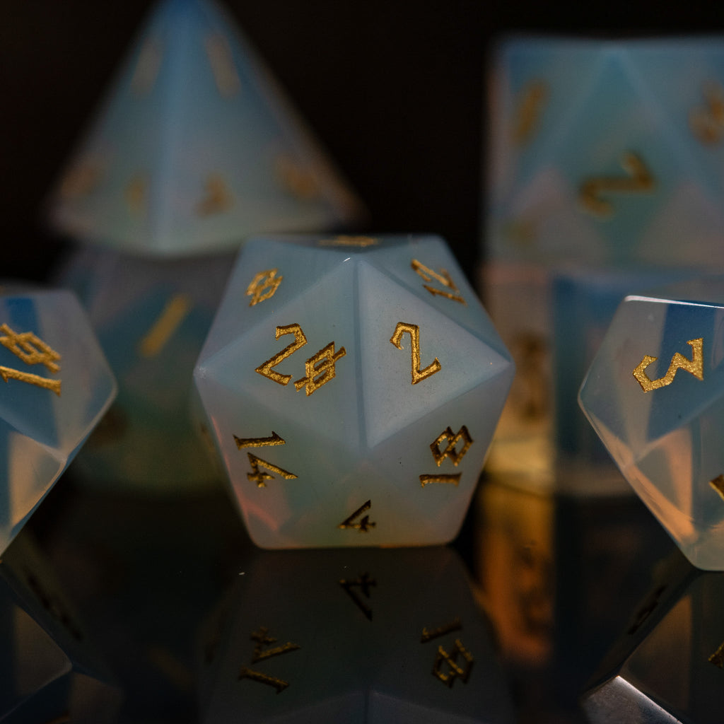 A collection of hand-carved, opalescent white gemstone dice with engraved numbers, displayed against a black background.
