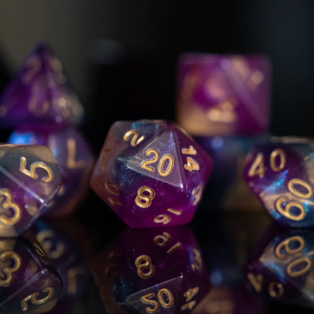 A set of acrylic dice with engraved numbers, featuring a gradient of purple to orange with gold numbering.