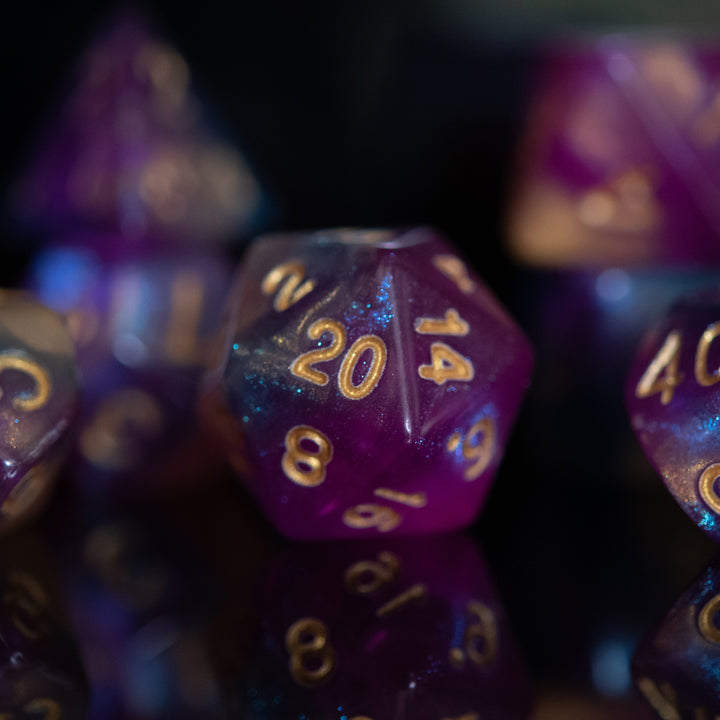 A set of acrylic dice with engraved numbers, featuring a gradient of purple to orange with gold numbering.