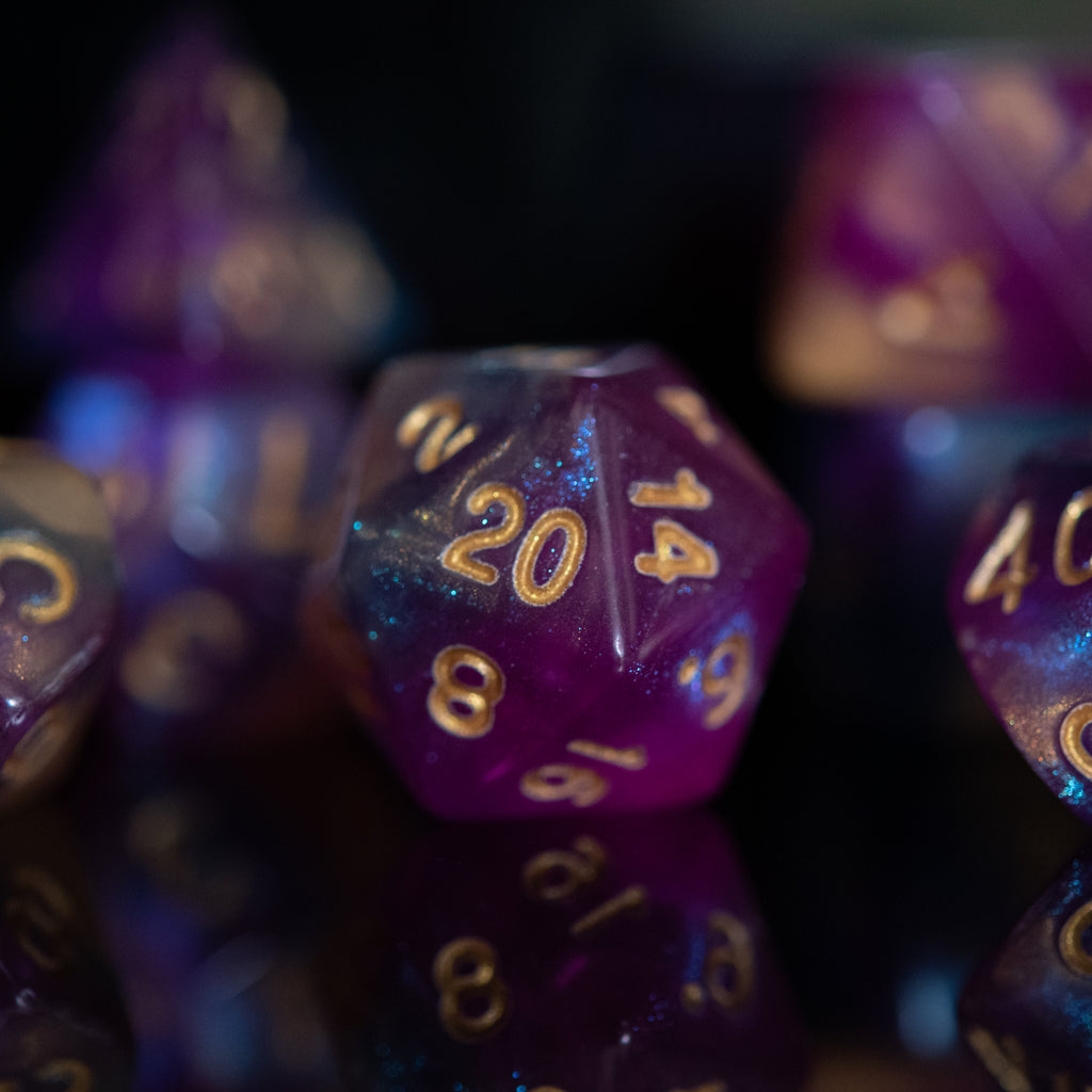 A set of acrylic dice with engraved numbers, featuring a gradient of purple to orange with gold numbering.