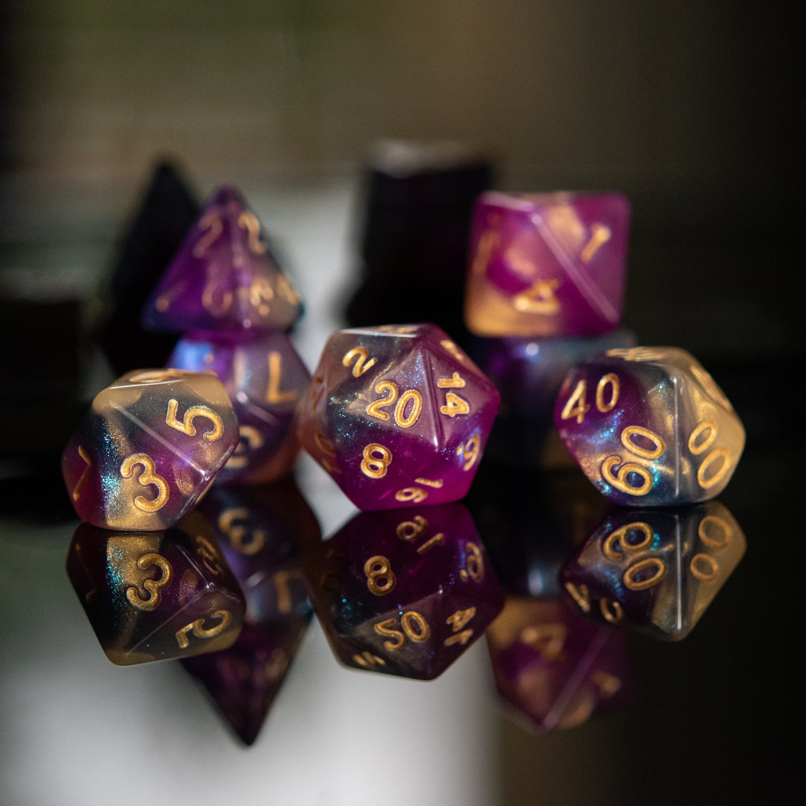 A set of acrylic dice with engraved numbers, featuring a gradient of purple to orange with gold numbering.