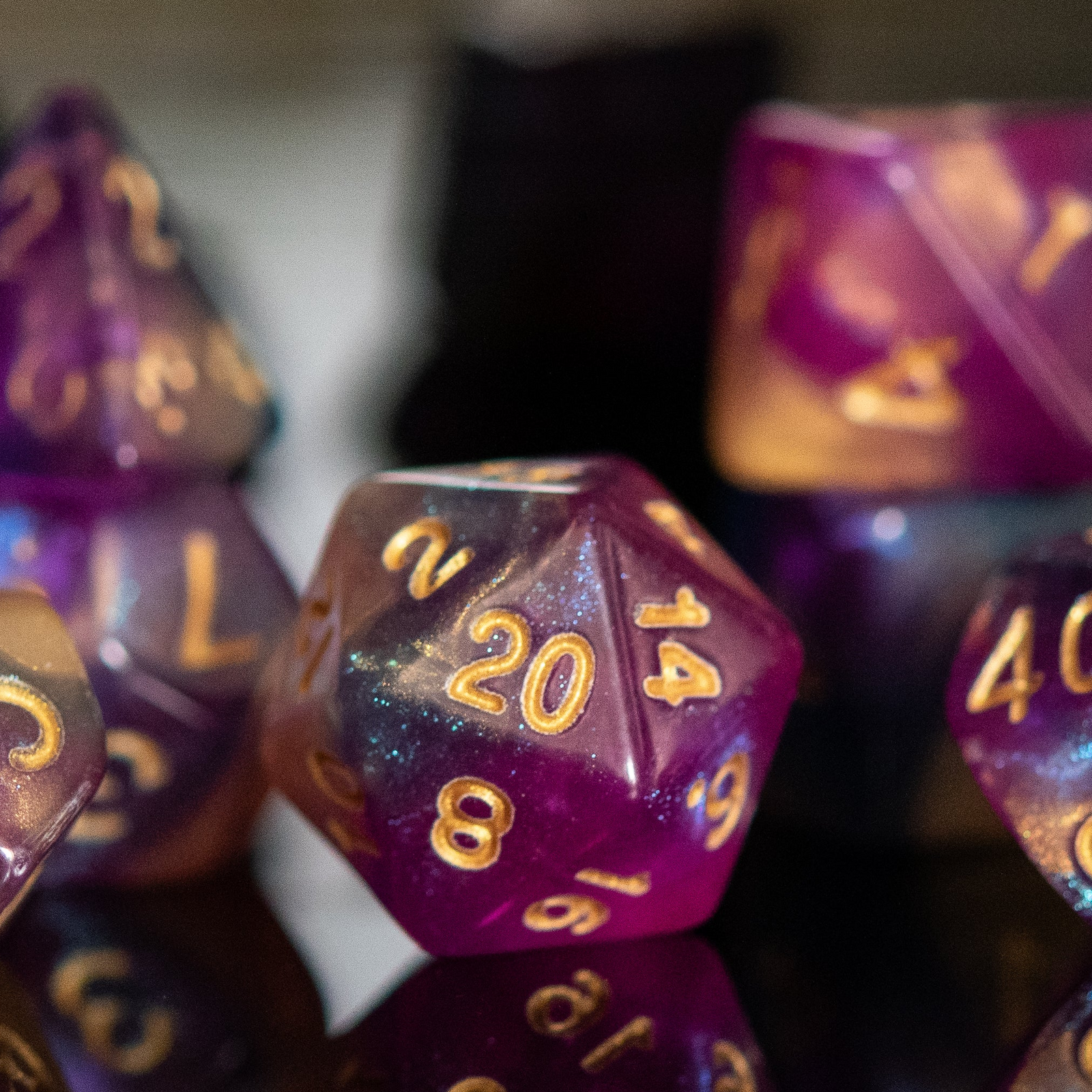 A set of acrylic dice with engraved numbers, featuring a gradient of purple to orange with gold numbering.