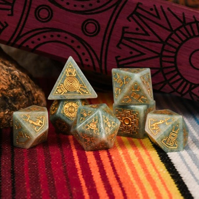 A set of hand-carved green amazonite stone dice with gold engravings, displayed on a colorful patterned fabric.