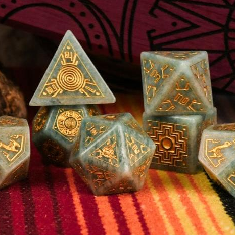 Set of green polyhedral dice with gold engravings on a colorful fabric background