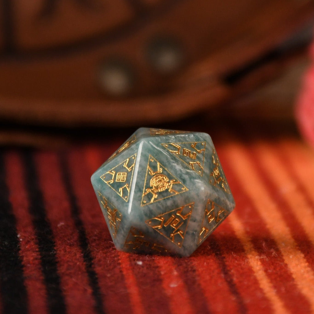 A set of hand-carved green amazonite stone dice with gold engravings, displayed on a colorful patterned fabric.