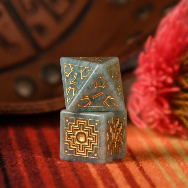 A set of hand-carved green amazonite stone dice with gold engravings, displayed on a colorful patterned fabric.