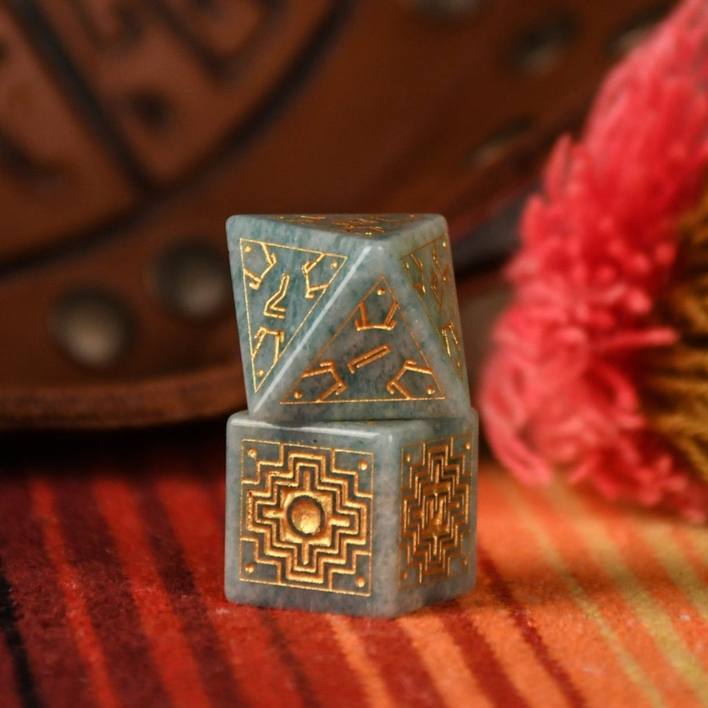 A set of hand-carved green amazonite stone dice with gold engravings, displayed on a colorful patterned fabric.