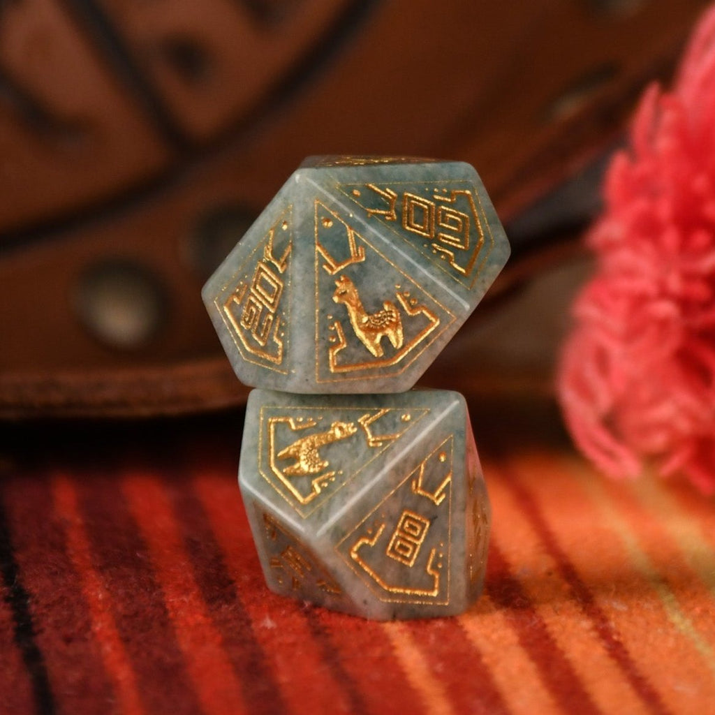 A set of hand-carved green amazonite stone dice with gold engravings, displayed on a colorful patterned fabric.