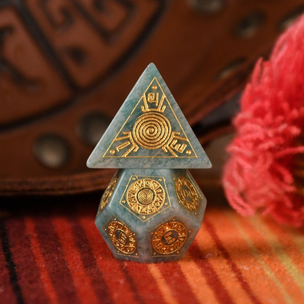 A set of hand-carved green amazonite stone dice with gold engravings, displayed on a colorful patterned fabric.