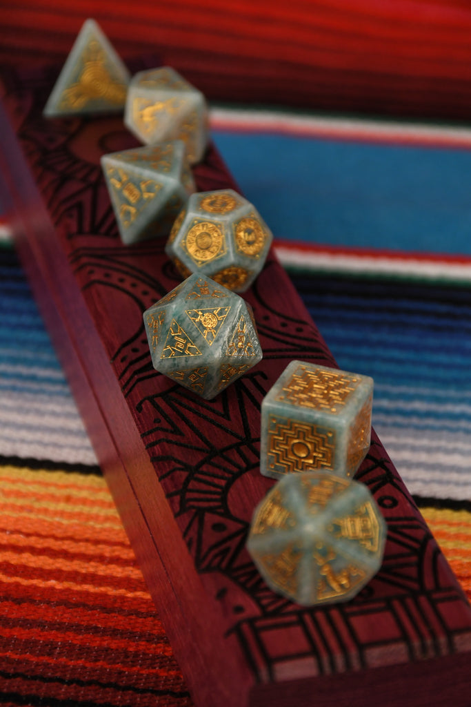 A set of hand-carved green amazonite stone dice with gold engravings, displayed on a colorful patterned fabric.