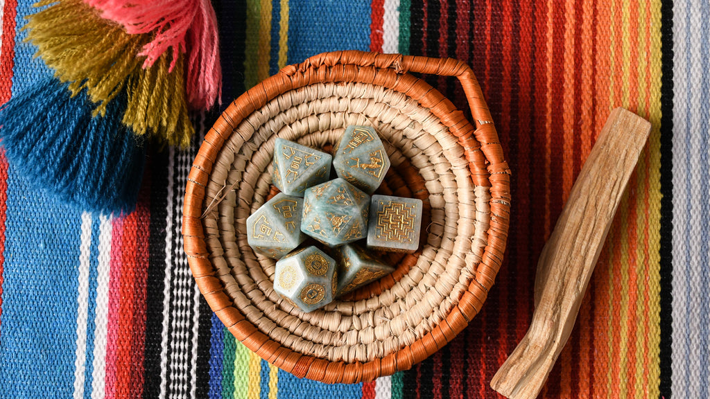 A set of hand-carved green amazonite stone dice with gold engravings, displayed on a colorful patterned fabric.