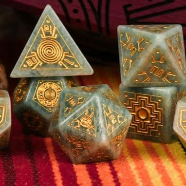 A set of hand-carved green amazonite stone dice with gold engravings, displayed on a colorful patterned fabric.