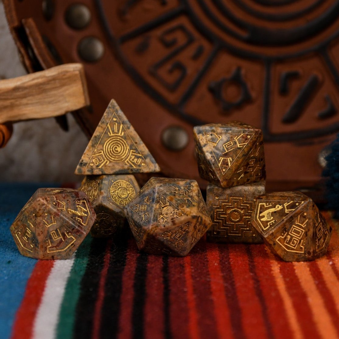 A set of hand-carved Peruvian Leopard Jasper stone dice, featuring engraved patterns and numbers, displayed on a colorful fabric.