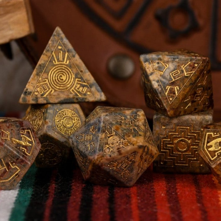 A set of hand-carved Peruvian Leopard Jasper stone dice, featuring engraved patterns and numbers, displayed on a colorful fabric.