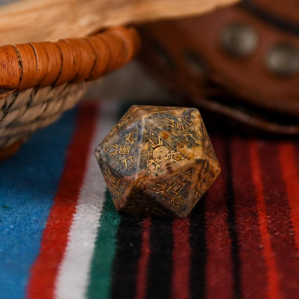A set of hand-carved Peruvian Leopard Jasper stone dice, featuring engraved patterns and numbers, displayed on a colorful fabric.