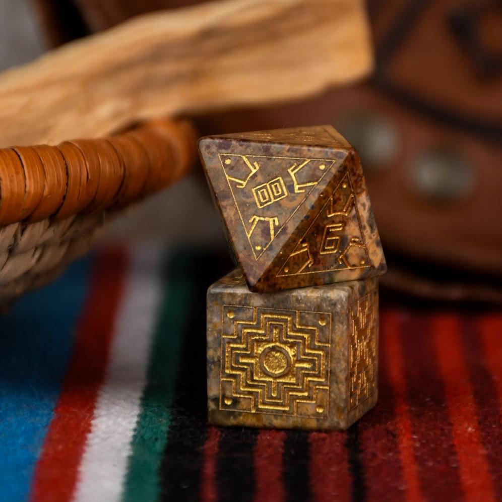 A set of hand-carved Peruvian Leopard Jasper stone dice, featuring engraved patterns and numbers, displayed on a colorful fabric.