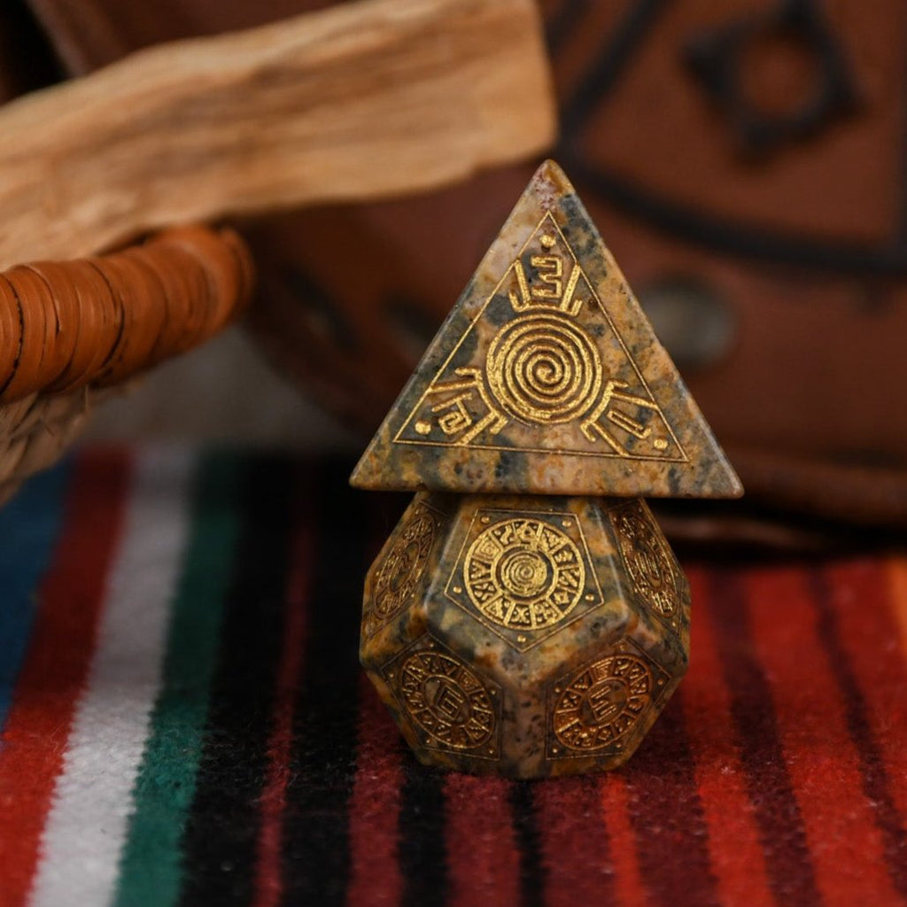 A set of hand-carved Peruvian Leopard Jasper stone dice, featuring engraved patterns and numbers, displayed on a colorful fabric.