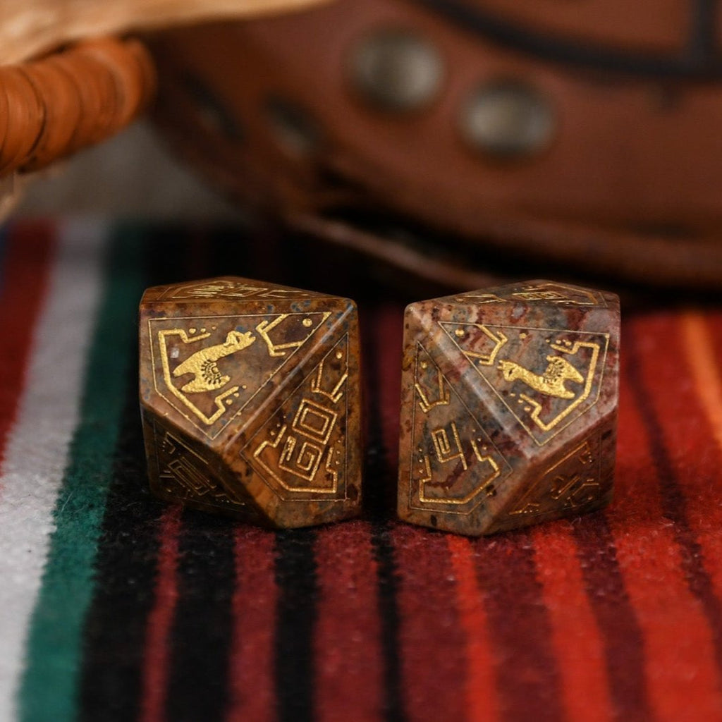 A set of hand-carved Peruvian Leopard Jasper stone dice, featuring engraved patterns and numbers, displayed on a colorful fabric.