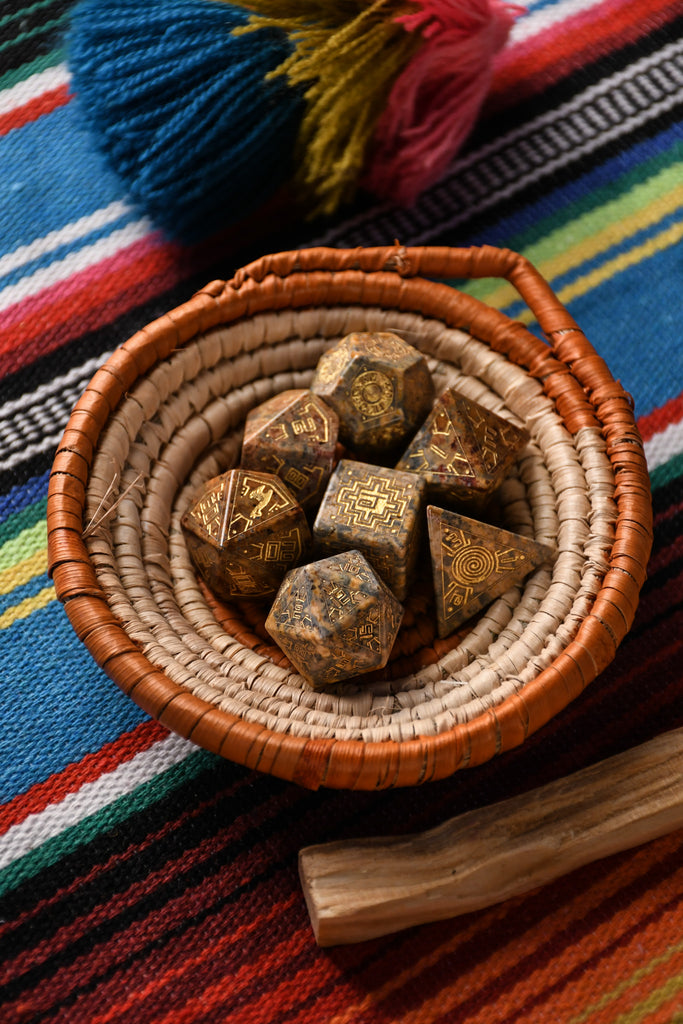 A set of hand-carved Peruvian Leopard Jasper stone dice, featuring engraved patterns and numbers, displayed on a colorful fabric.
