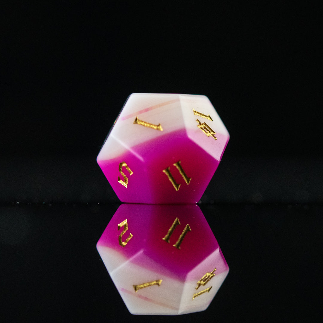 A set of pink agate stone dice with engraved numbers, polished and displayed on a reflective surface.