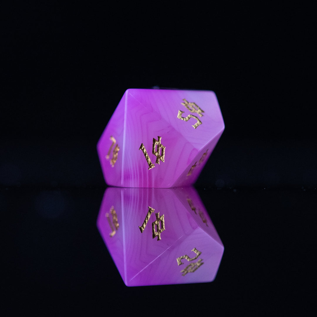 A set of pink agate stone dice with engraved numbers, polished and displayed on a reflective surface.