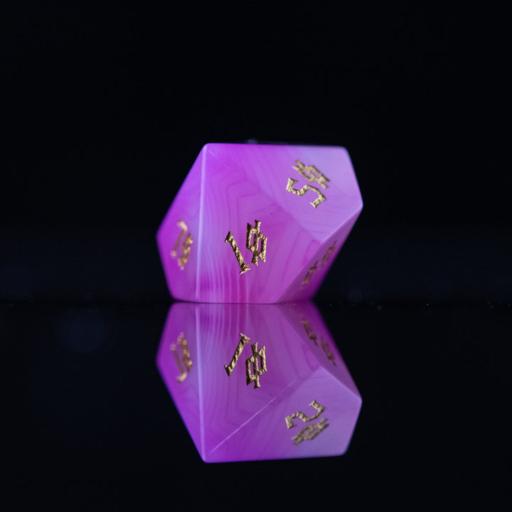 A set of pink agate stone dice with engraved numbers, polished and displayed on a reflective surface.