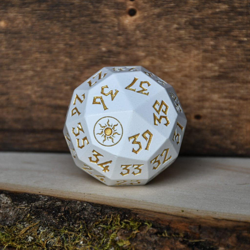 A single white d40 metal dice with golden engraved numbers and iconography, resting on a wooden surface.