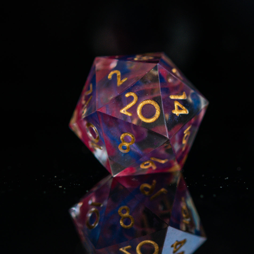 A set of colorful sharp-edged resin dice with hand-painted numbers, featuring a multicolor finish with gold numbers, displayed on a reflective surface.