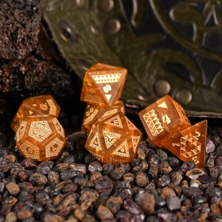 A set of Polynesian Lava Glass dice with Polynesian designs engraved on them, displayed on a bed of dark pebbles.