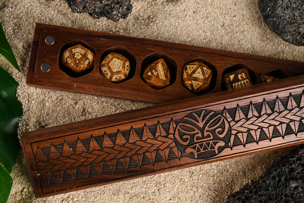 A set of Polynesian Lava Glass dice with Polynesian designs engraved on them inside a wooden dnd dice vault box