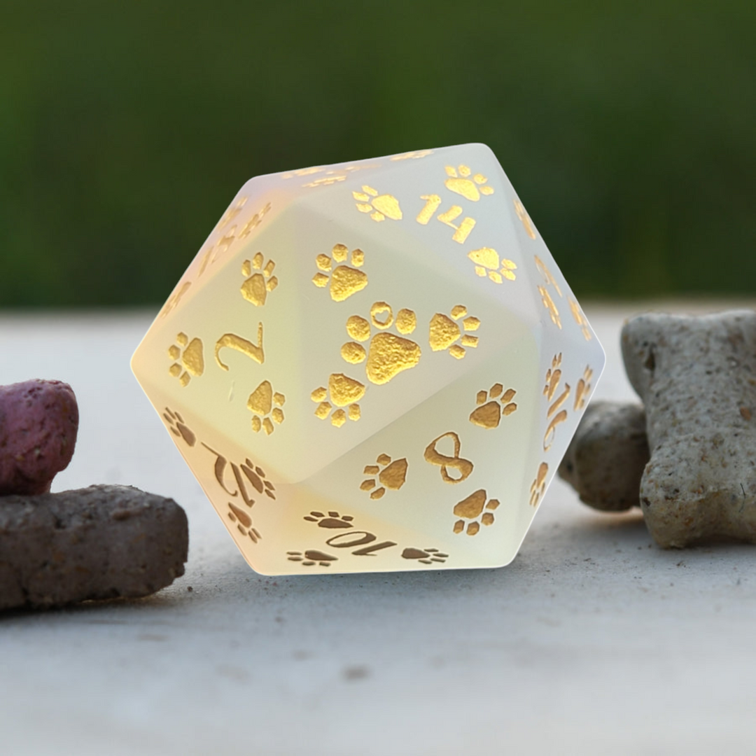 A frosted prism glass 30mm D20 dice with puppy paw prints and engravings, displayed on a natural stone surface.