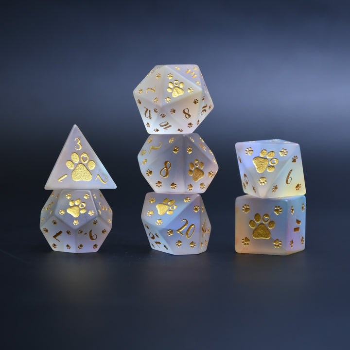 A set of frosted glass dice with gold paw prints and numbers, including various shapes typical for role-playing games like D&amp;D.