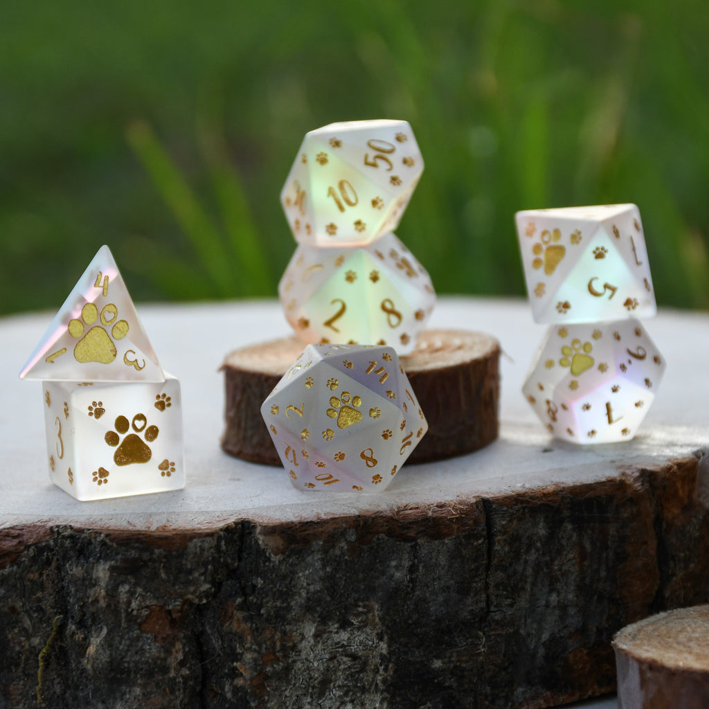 A set of frosted glass dice with gold paw prints and numbers, including various shapes typical for role-playing games like D&D.