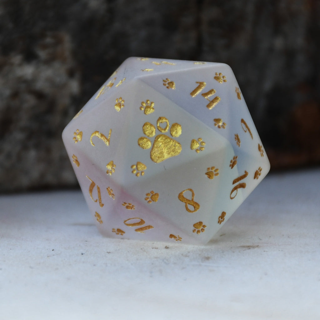 A set of frosted glass dice with gold paw prints and numbers, including various shapes typical for role-playing games like D&D.