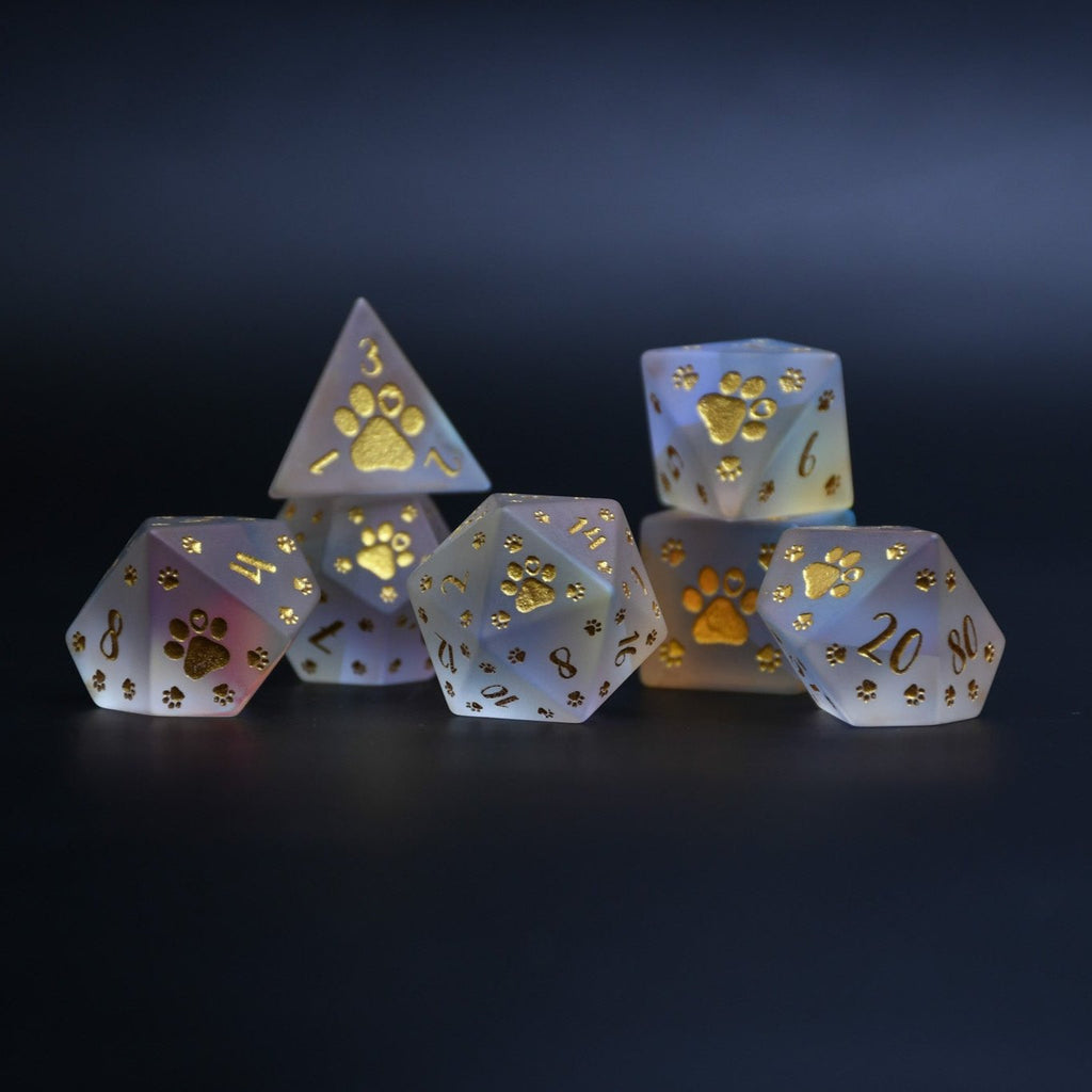 A set of frosted glass dice with gold paw prints and numbers, including various shapes typical for role-playing games like D&D.