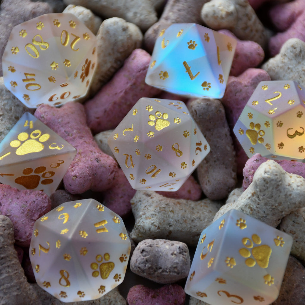 A set of frosted glass dice with gold paw prints and numbers, including various shapes typical for role-playing games like D&D.