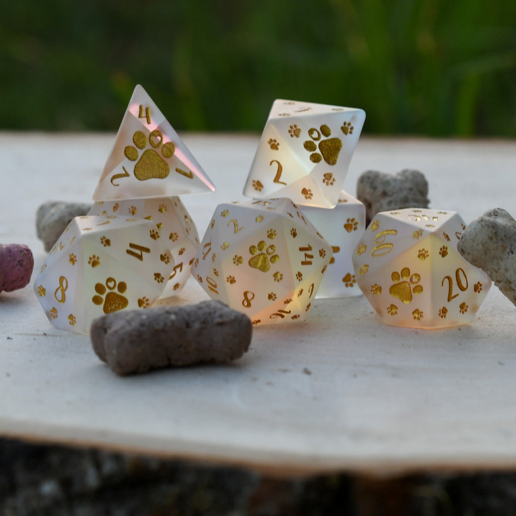 A set of frosted glass dice with gold paw prints and numbers, including various shapes typical for role-playing games like D&D.