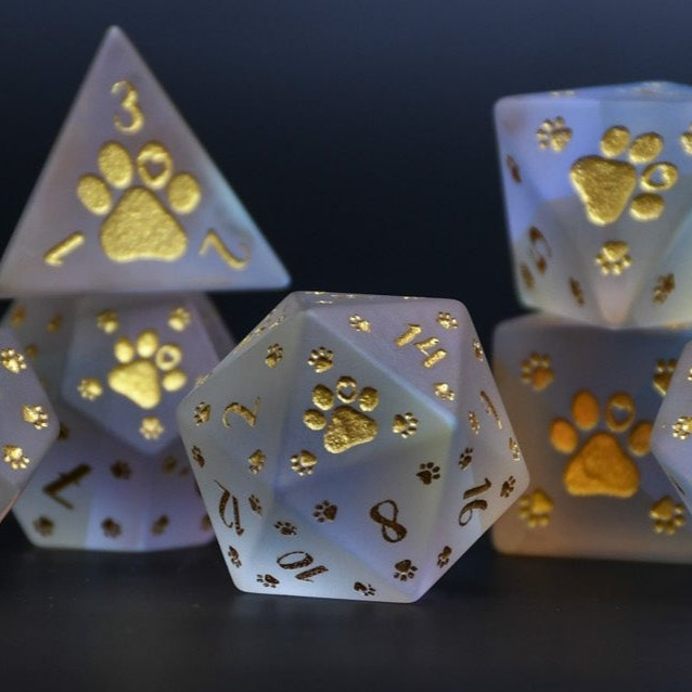 A set of frosted glass dice with gold paw prints and numbers, including various shapes typical for role-playing games like D&D.