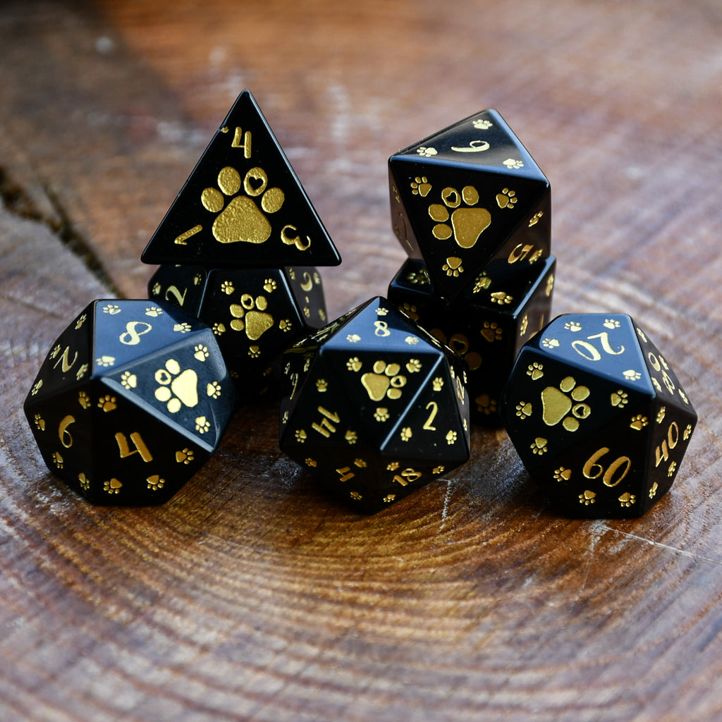 Black polyhedral dice set with gold paw prints on a wooden surface