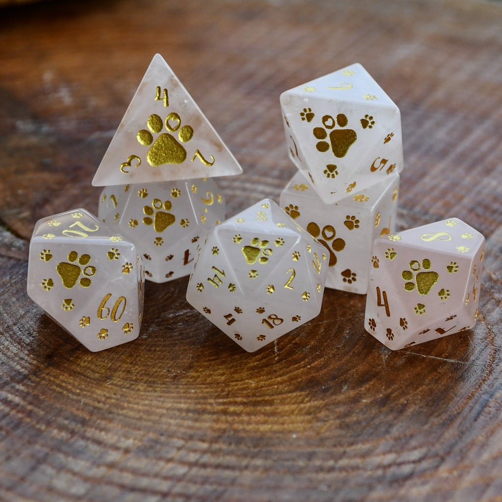 Puppy Paws Rose Quartz Dice Set with gold paw prints and numbers on a wooden surface