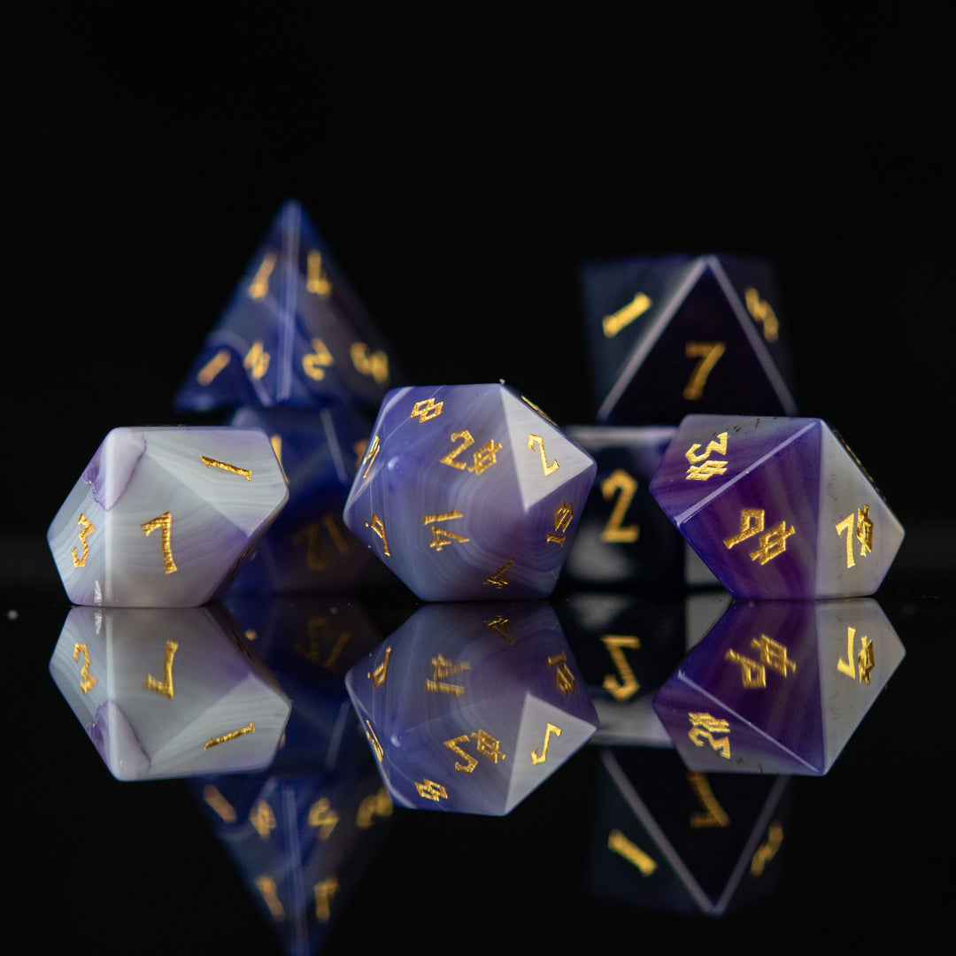 A set of purple agate stone dice with engraved numbers, displayed on a reflective surface.