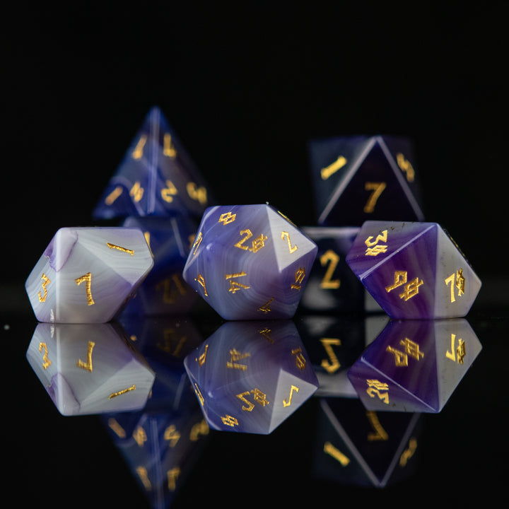 A set of purple agate stone dice with engraved numbers, displayed on a reflective surface.