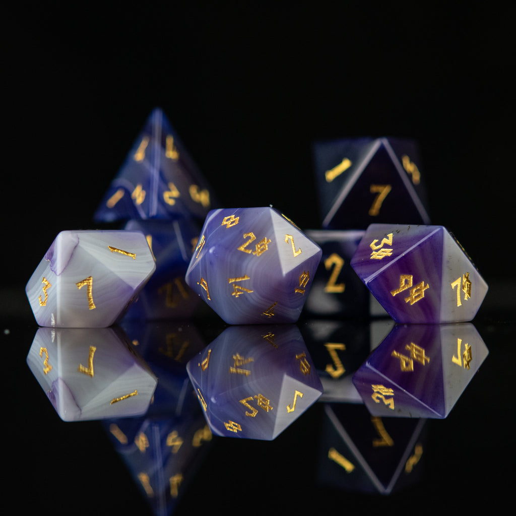 A set of purple agate stone dice with engraved numbers, displayed on a reflective surface.