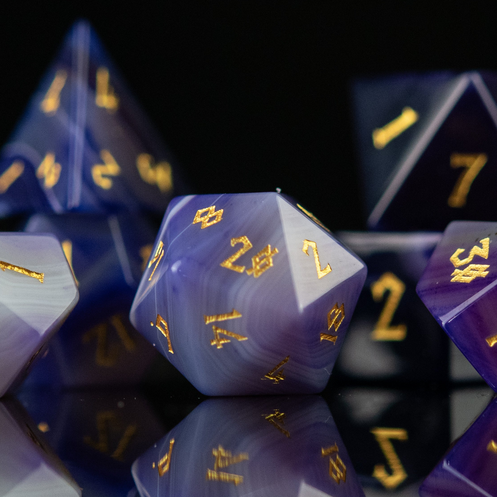 A set of purple agate stone dice with engraved numbers, displayed on a reflective surface.