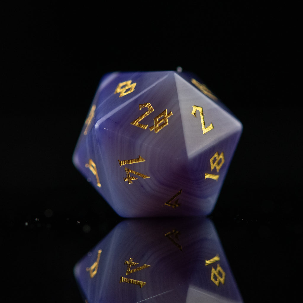 A set of purple agate stone dice with engraved numbers, displayed on a reflective surface.