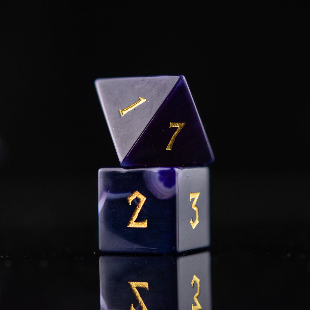 A set of purple agate stone dice with engraved numbers, displayed on a reflective surface.