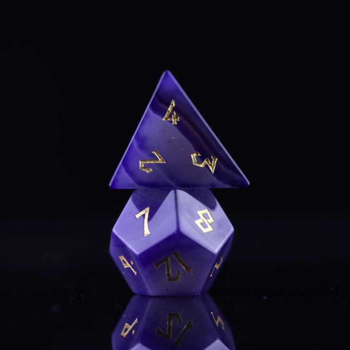 A set of purple agate stone dice with engraved numbers, displayed on a reflective surface.