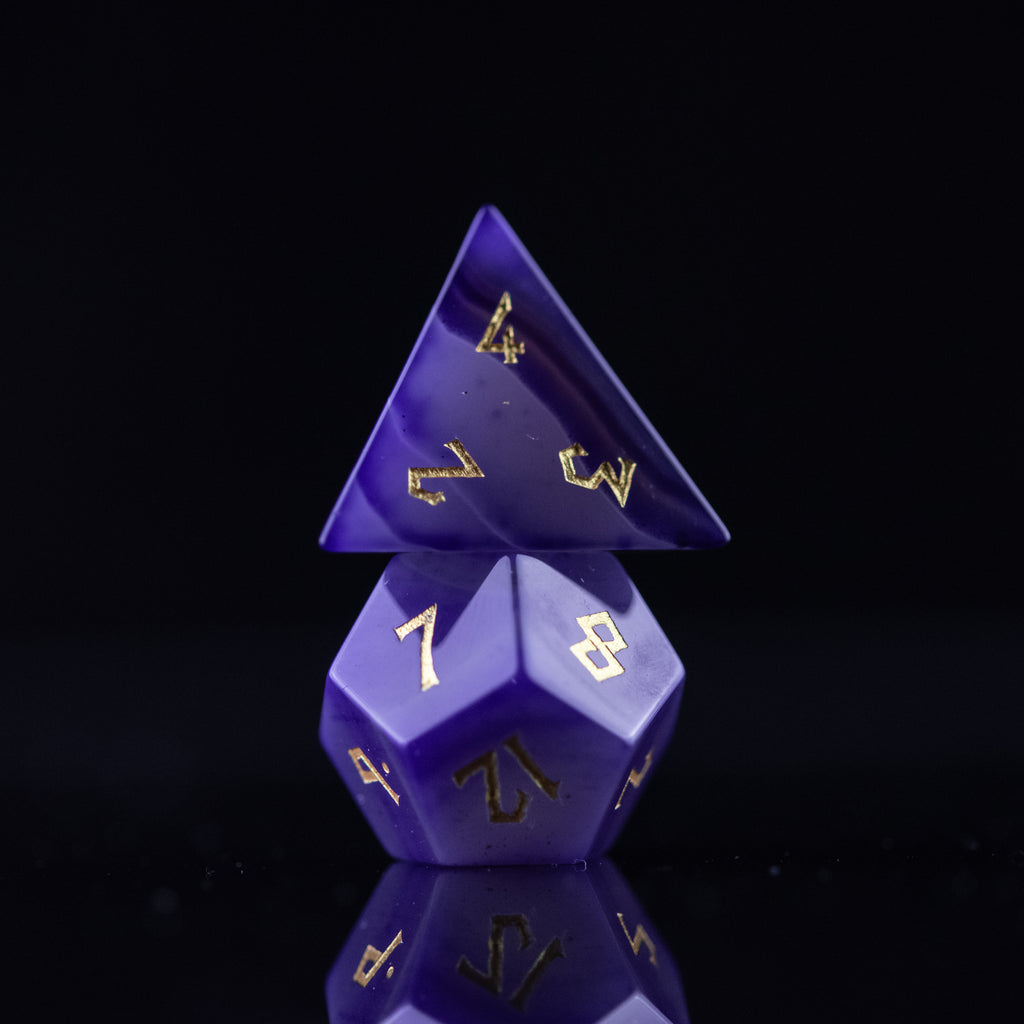 A set of purple agate stone dice with engraved numbers, displayed on a reflective surface.